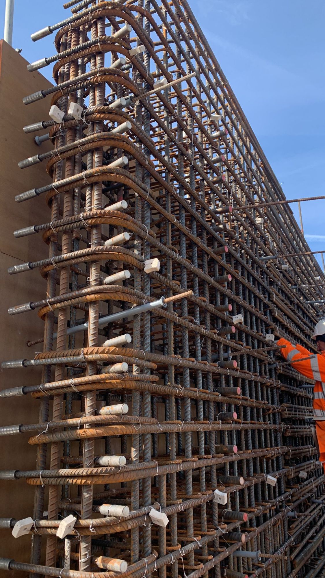 Close-up of a tall wall reinforcement cage with mechanical couplers and a fixer in PPE