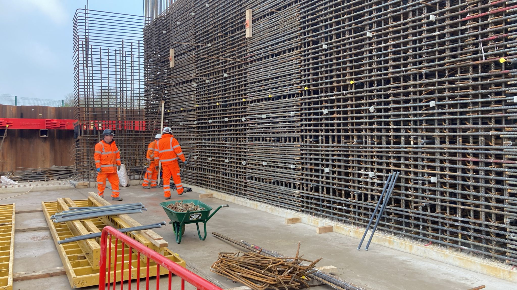 Two Quick-Steel-Fix fixers in orange PPE on site in front of a tall wall reinforcement cage